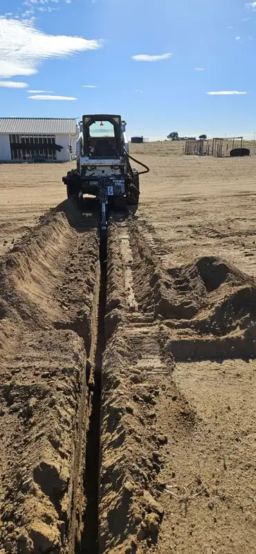 Bobcat trenching a long line across a dirt lot
