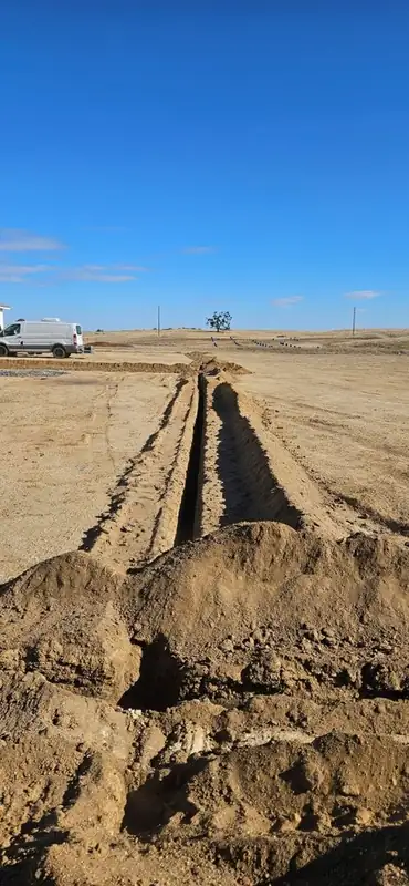 Freshly dug trench line with excavated soil across an open field