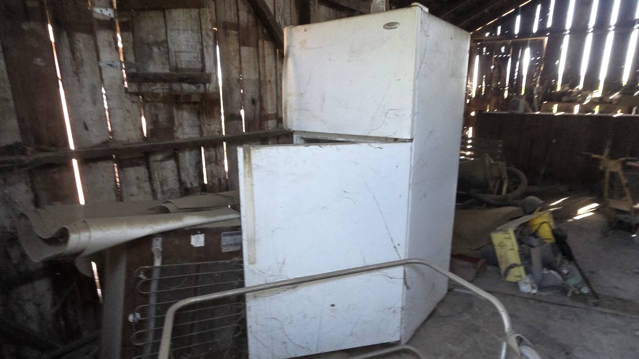 Old white refrigerator waiting in a Central Valley barn for appliance removal by Superior Hauling